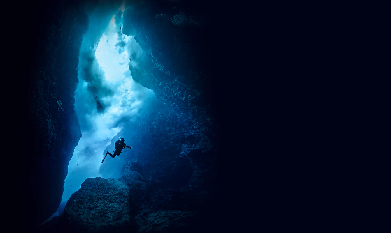 A diver descends through a sunlit underwater canyon in the Red Sea