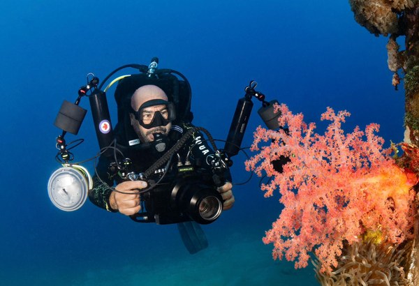 Yazan Alsaed, founder and PADI instructor at Sea Guard, diving with an underwater camera beside a reef